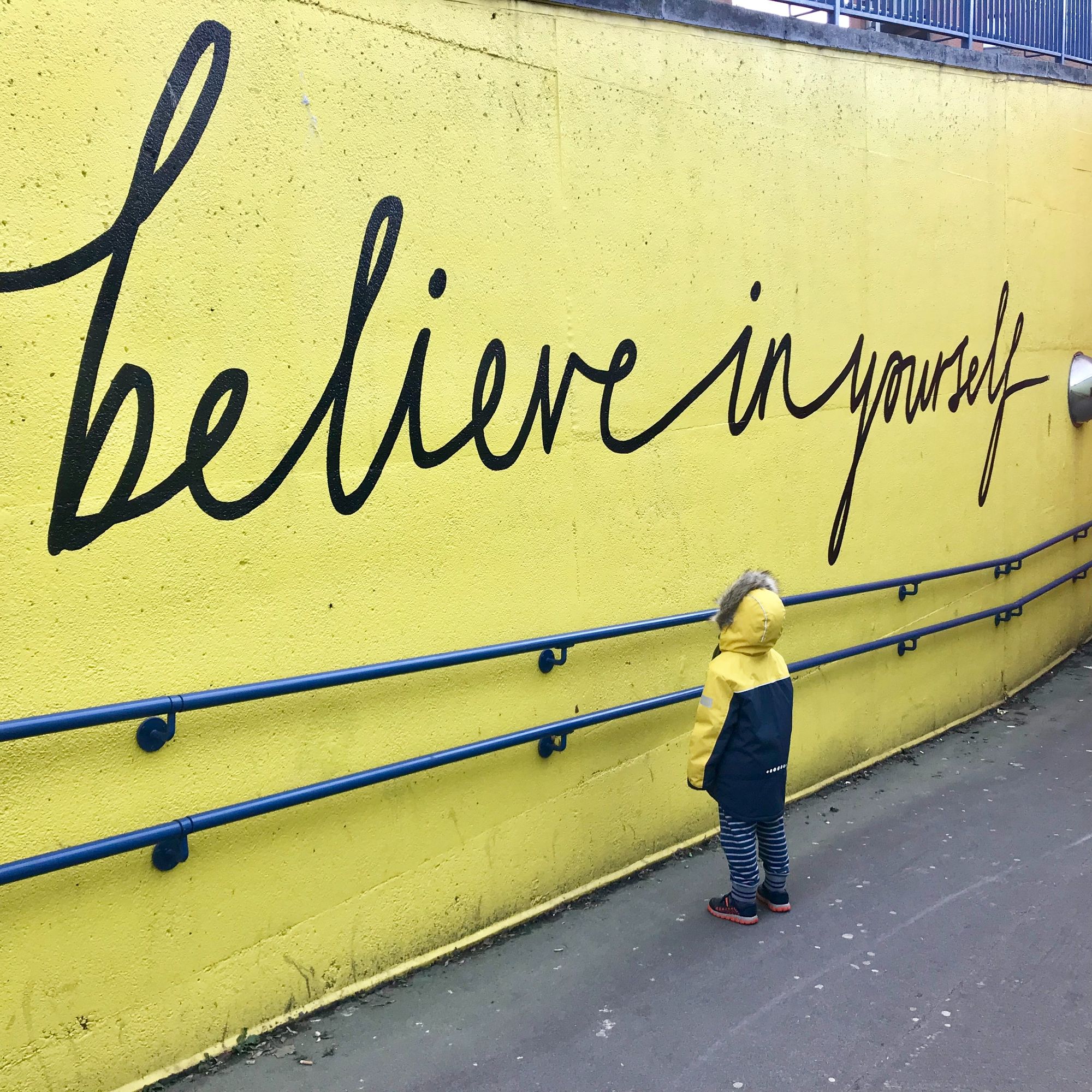 dziecko patrzące na mur z napisem: believe in yourself